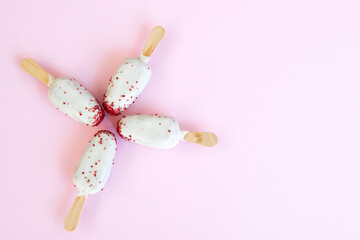 Cake on a popsicle  stick, white with red sprinkles as a flat lay on a pink background.
