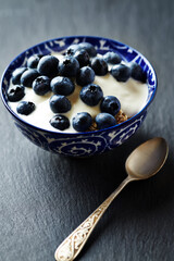 Bowl of granola with yogurt and bilberries. Concept for a tasty and healthy meal. Dark stone background. Close up. Copy space. 	
