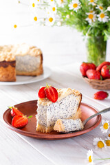 Homemade cottage cheese poppy seed cake on an wooden table with flowers and strawberries on a background