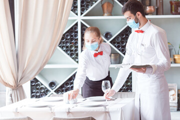 the waiter serves a table in a cafe in a protective mask.