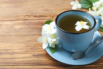 Cup of tea and fresh jasmine flowers on wooden table. Space for text