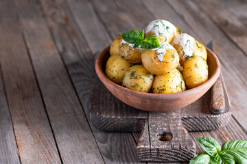 Young roasted potatoes with dill in a ceramic bowl on a wooden table. Place for text