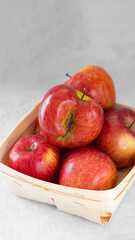 Red fresh organic apples in small wooden pottle with ugly fruit on top. On grey cement background. Buying imperfect product to reduce waste. Sustainable consumption. Vertical banner. Eco trend.