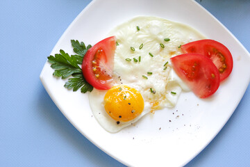 Coocked chircken egg on a plate, with a parsley leaf and tomate.