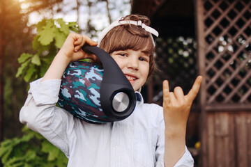 Child with portable speaker enjoying the music in park, outdoors. Kid listening music by wireless...