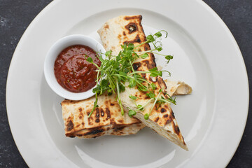 Pita bread with suluguni cheese, sauce, microgreen, on a white plate, on dark concrete. Cooked on the grill