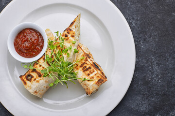Pita bread with suluguni cheese, sauce, microgreen, on a white plate, on dark concrete. Cooked on the grill