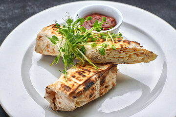 Pita bread with suluguni cheese, sauce, microgreen, on a white plate, on dark concrete. Cooked on the grill
