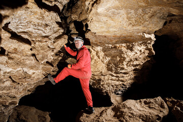 Man walking and exploring dark cave with light headlamp underground. Mysterious deep dark, explorer discovering mystery moody tunnel looking on rock wall inside.