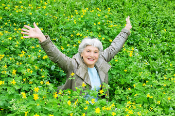 Happy beautiful elderly woman sitting on a glade of yellow flowers in spring