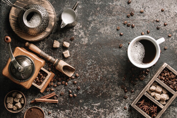 Coffee cup with coffee grinder and coffee beans on dark textured background.