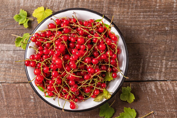 fresh ripe red currants in a bowl on old wooden table, top view.