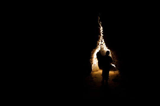 Man walking and exploring dark cave with light headlamp underground. Mysterious deep dark, explorer discovering mystery moody tunnel looking on rock wall inside.