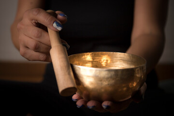 Fototapeta na wymiar Woman practicing sound healing therapy with a golden Tibetan singing bowl, focusing on creating a serene atmosphere for meditation and stress relief. 