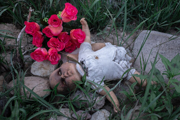 Un muñeco viejo, abandonado, junto a unas rosas bellas y sintéticas, el contraste perfecto entre lo bello y lo imperfecto.