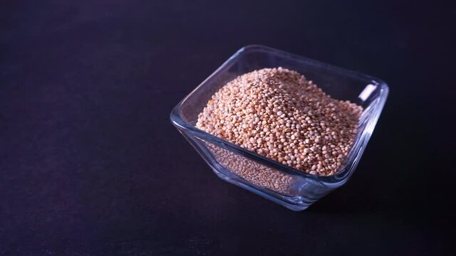 Quinoa amarilla org&aacute;nica vertida en recipiente de cristal sobre mesa negra