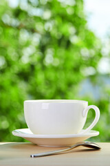 a white cup with tea or  tasty coffee beverage. hot drink over beautiful nature background. copy space. vertical orientation.