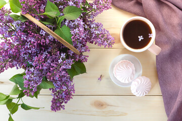 Obraz na płótnie Canvas Cup of tea or coffee with sweet pink marshmallows and bouquet of lilac in a basket on wooden background. Breakfast in the morning.