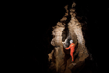 Obraz premium Man walking and exploring dark cave with light headlamp underground. Mysterious deep dark, explorer discovering mystery moody tunnel looking on rock wall inside.