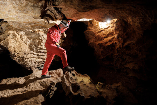 Man walking and exploring dark cave with light headlamp underground. Mysterious deep dark, explorer discovering mystery moody tunnel looking on rock wall inside.