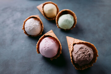 Ice cream background. Set of various flavored scoops in waffle cones on dark table. Food, summer dessert, refreshment concept