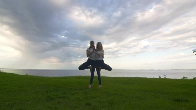 Two women in activewear pposing on the camera and showing together yoga Tree pose Vrksasana Vriksasana