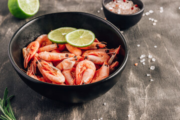 Top view of bowl with boiled shrimps with lime in black bowl on dark background.