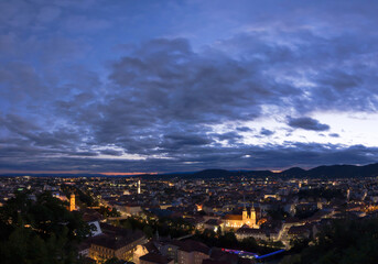 City lights of Graz and Mariahilfer church (Mariahilferkirche), view from the Shlossberg hill, in Graz, Styria region, Austria, after sunset. Panoramic view.