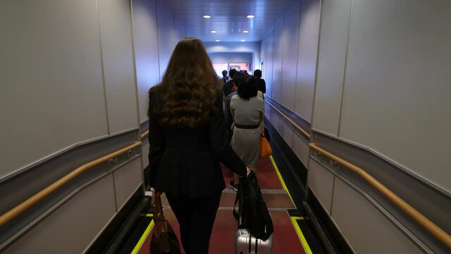 Passengers boarding to plane, people slowly walk, economy class queue at jet bridge. Woman go at end of line with trolley case, first person view camera follow behind