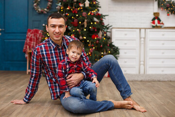 Little boy with his father near fir-tree. Christmas celebration. Boy with Dad weared in red checkered shirts. New year eve