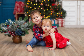 Fototapeta na wymiar Little boy and girl near fir-tree. Christmas celebration. Sister and brother weared in red clothes. New year eve