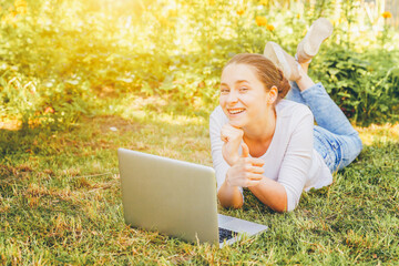 Mobile Office. Freelance business concept. Young woman lying on green grass lawn in city park working on laptop pc computer. Lifestyle authentic candid student girl studying outdoors