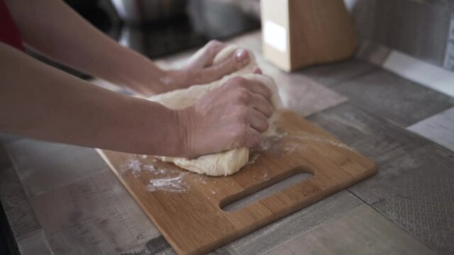 Female hands in flour kneading dough on a wooden board. Action. Close up of woman hands making bread or preparing dough for a pie, cooking and food concept.