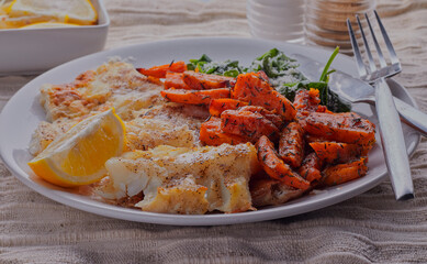 Healthy cod fillet, with spicy  potato wedges, garnished with lemon wedge.