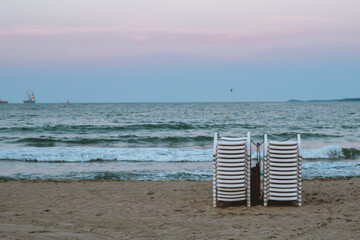 Stacked and locked to one another plastic beach chairs on a beach at sunset.