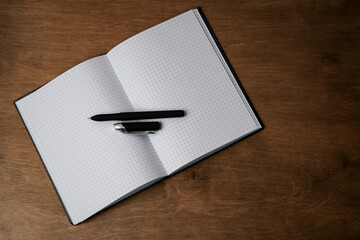 Open notepad in a cage on a wooden table with a pen. Open the notebook on the office desk. Outdoor notepad / diary with pen on old wooden brown table. Business concept, place for text