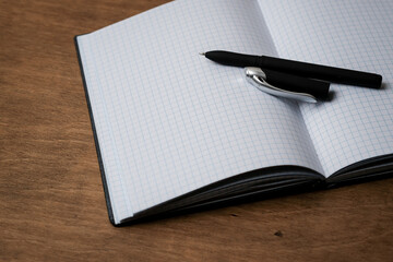 Open notepad in a cage on a wooden table with a pen. Open the notebook on the office desk. Outdoor notepad / diary with pen on old wooden brown table. Business concept, place for text