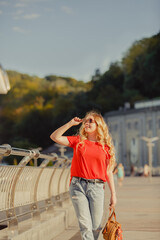 Beautiful girl walk in the summer Kiev City. Young woman tourist on a street. Street style portrait. Stylish girl near a river weared in red casual outfit. Life style. Local tourism. Srteet walk. 