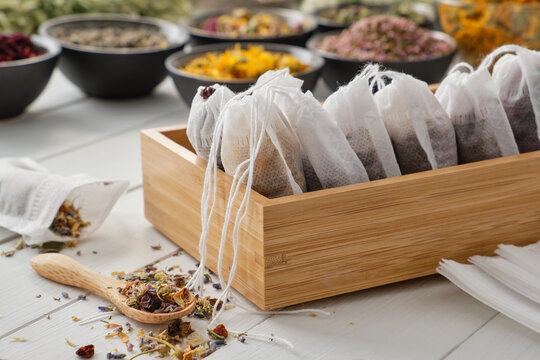 Wooden box of tea bags filled with dry medicinal herbs and flowers. Bowls of medicinal plants on background. Alternative medicine