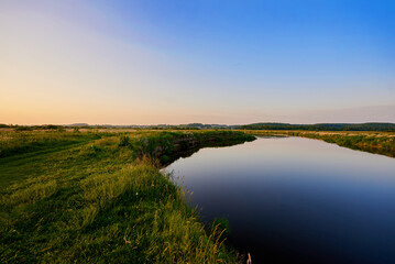 Fototapeta na wymiar Beautiful blue Narew river flowing next to the green grass near Łomża