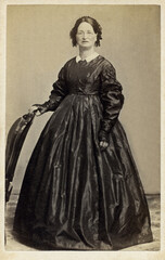 Fototapeta na wymiar Antique 1860's Civil War Era Carte De Vista CDV Photo of Older Woman Standing next to Chair and is wearing a pair of eye glasses.