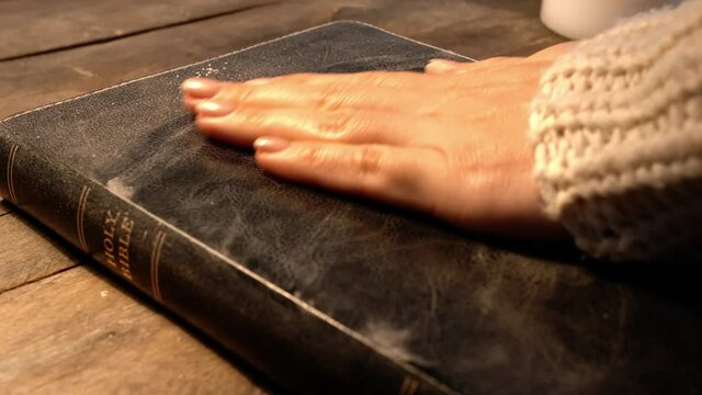 Woman cleaning dust off Holy Bible on table, closeup