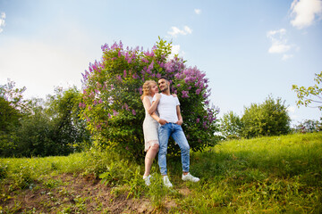 Young man and woman couple near a blooming lilac bush. Tender holding each other. Spring lovestory. Blonde-haired girl with curled hairs and man weared in casual. Young family