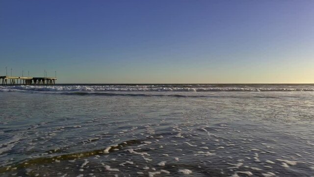 Low angle shot of Venice Beach at sunset with waves washing up on the sandy shoreline in Summer in Los Angeles California - Static Shot