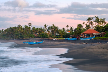 Obraz premium Traditional indonesian fishing boats on the black beach of bali island. Dawn on the beach. Palm trees and the ocean at dawn.