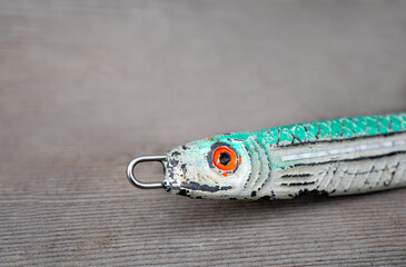 Close up of old fishing lure. Focus on colorful head with red eyes and blue green top side. Fishing lure is well used and banged up. Soft wood background.
