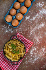 uncooked pasta in fusilli-type screws served in a black pot with forks on a rusty metal table decorated with parsley accompanied by a basket of fresh eggs