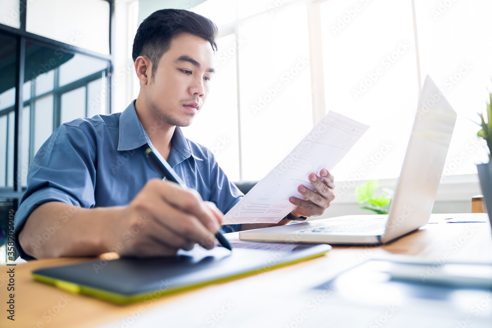 Fototapete Working from home web designing graphical user interface UX UI, home office using computer laptop and pen sketching graphics tablet, using draft ideas and plans on paper drawing, asian man quarantine