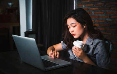 Asian businesswoman working late night tired sleepy overwork drinking coffee using computer laptop technology freelance business plan strategy work from home modern office during coronavirus COVID-19