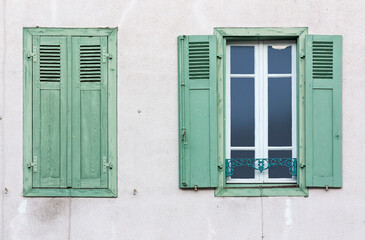 A window with open wooden shutters and window with closed shutters on a plastered wall